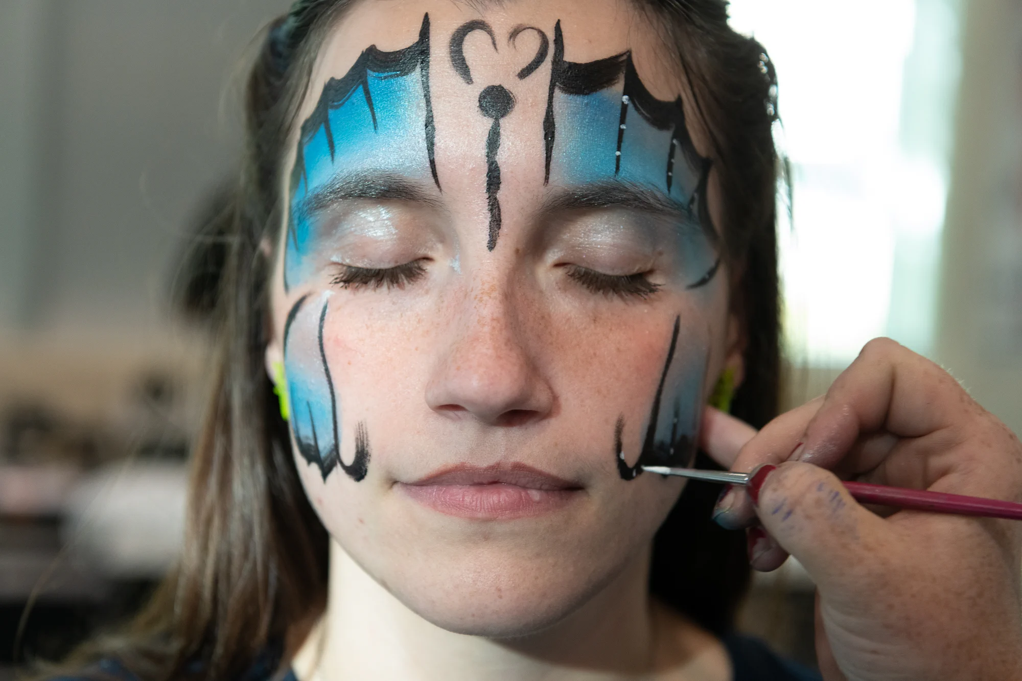 A student closes her eyes as an artist paints an intricate blue and black design on her face during UIS Homecoming.