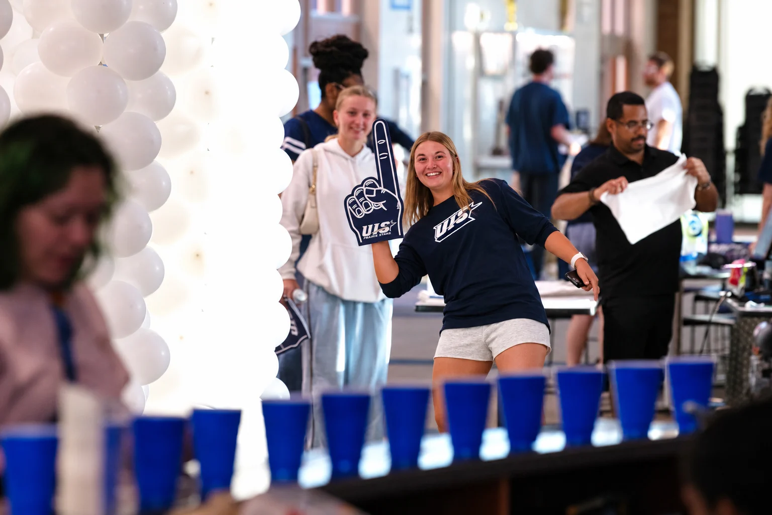 A UIS student holds a Prairie Stars foam finger while playing a game with blue cups during Homecoming festivities.
