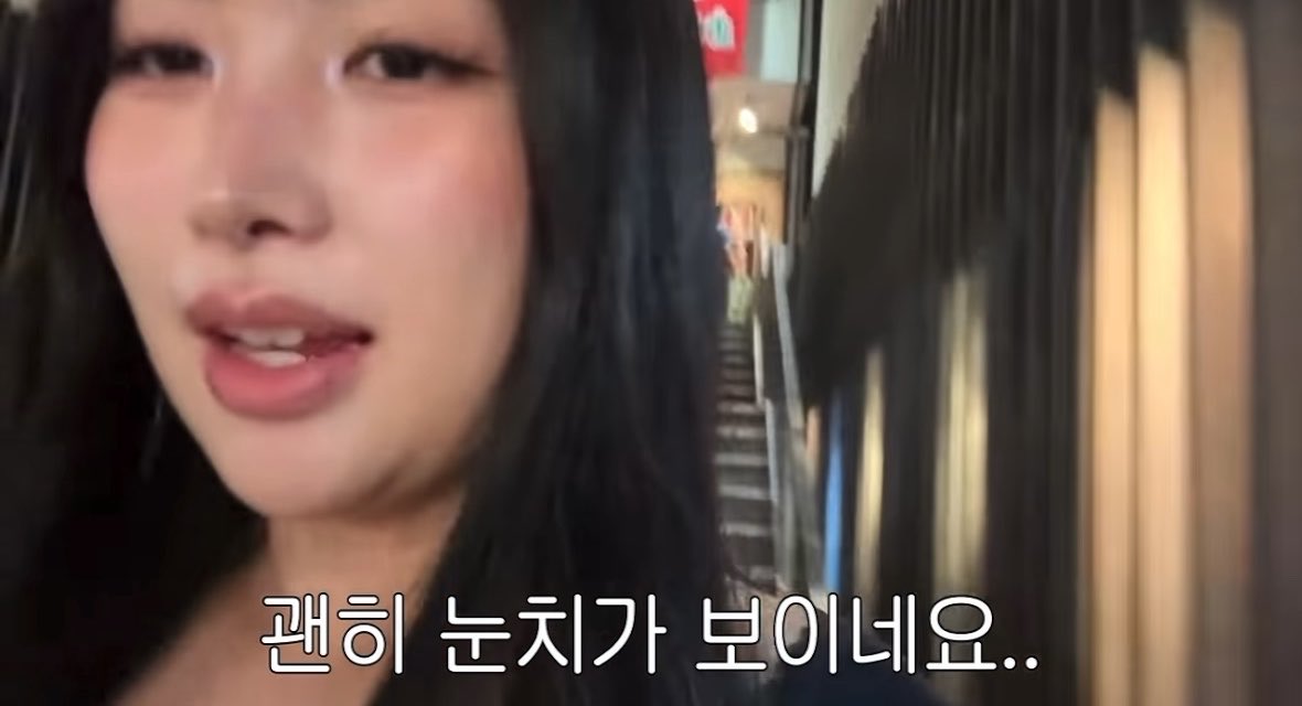 A close-up of a young woman speaking on camera with Korean subtitles at the bottom reading "괜히 눈치가 보이네요..".