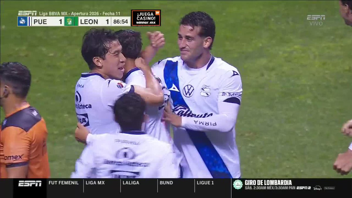 Puebla players embrace on the field during a Liga BBVA MX Apertura 2026 match against León, tied 1-1 at 86:54 on the ESPN broadcast, with a player in the foreground holding up a match jersey displaying the number 9, signed and framed as a keepsake to commemorate the moment.