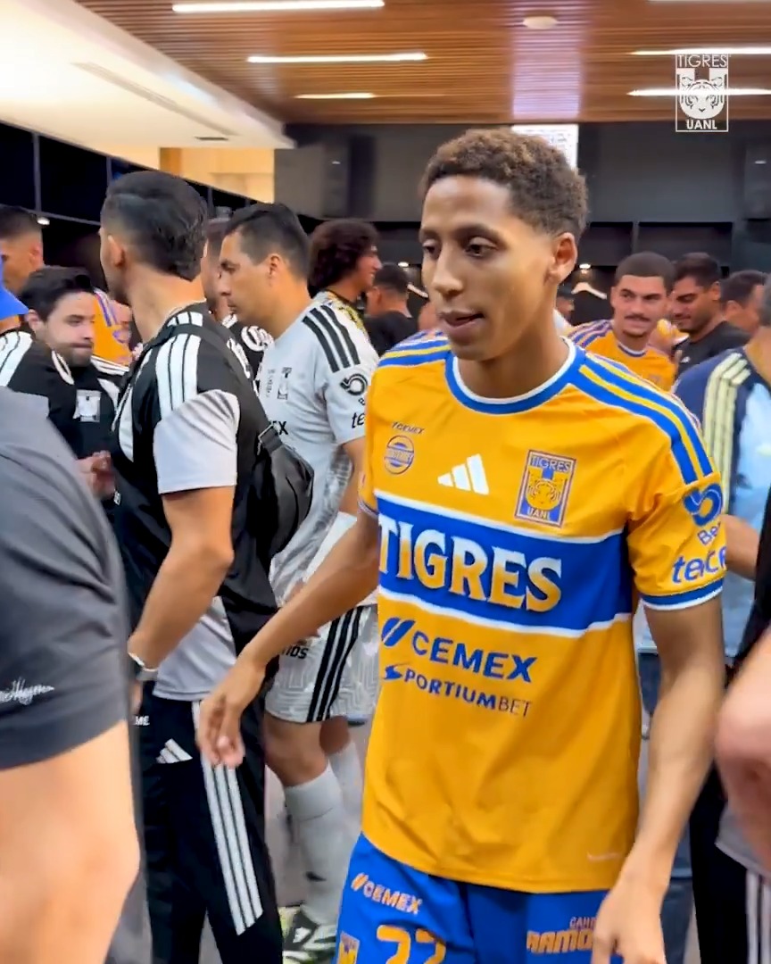 A young soccer player wearing the yellow and blue Tigres jersey with "CEMEX" and "PORTIUMBET" sponsorships walks through a crowded locker room tunnel, while the "@CarnesRamos" caption celebrates the team with "1, 2, 3 and let's go Tigers!" — capturing the pre-game excitement of the Tigres UANL squad.