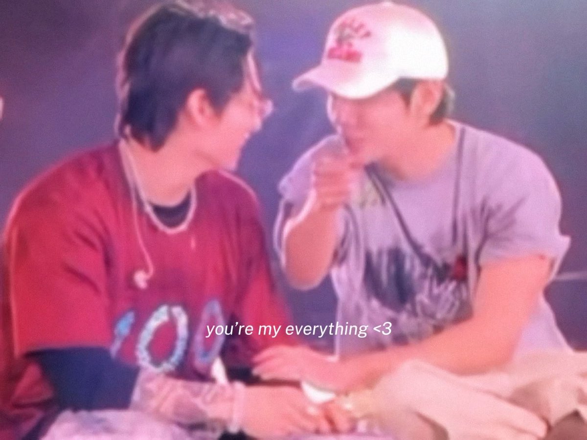 A blurry photo of two young men, one in a white cap and grey shirt touching the other's face, with the caption 'you're my everything <3'.