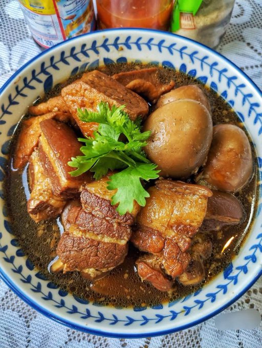 A bowl of braised pork belly with eggs in a savory soy-based sauce, garnished with fresh cilantro and served in a blue and white patterned bowl.