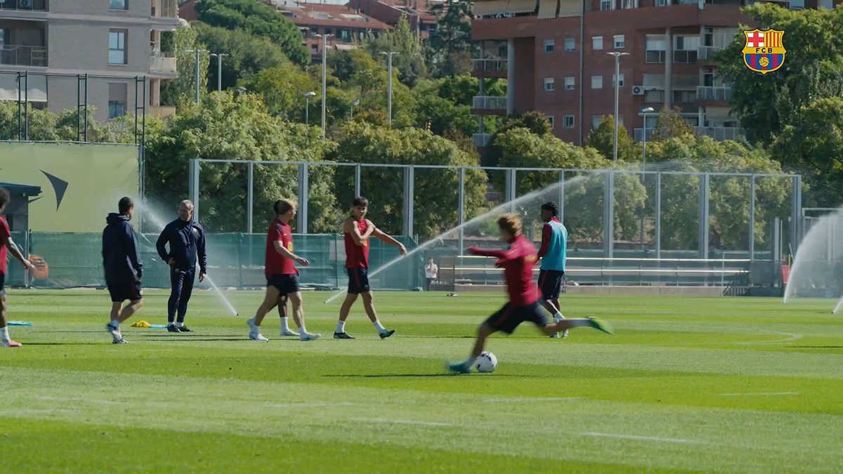 The FC Barcelona crest appears in the top right corner as players train on a sunlit pitch with sprinklers running, while one player in the foreground dribbles a ball to showcase the skill highlighted in the post about Pedri being a wizard with the ball.