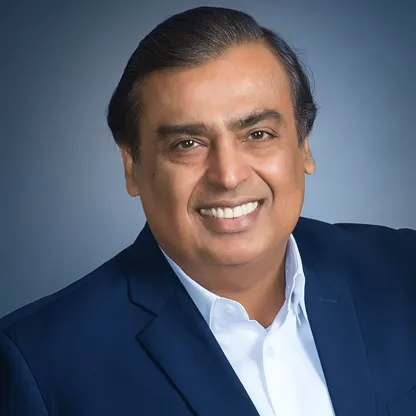 A professional headshot portrait of a smiling middle-aged man with dark hair, wearing a dark blue suit jacket over a light blue dress shirt against a gray background.