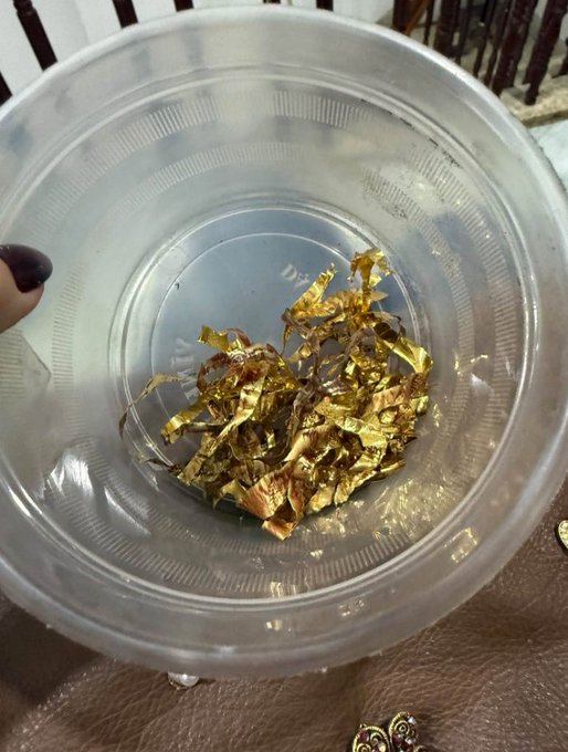 A close-up of a clear plastic container filled with small pieces of gold leaf.
