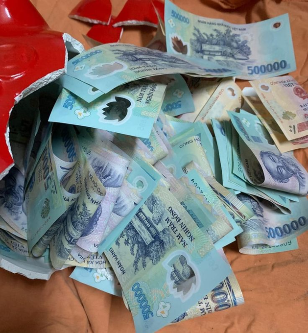 A pile of Vietnamese 500,000 dong banknotes spills out of a red envelope or container, displaying the blue and green currency notes scattered on an orange surface.
