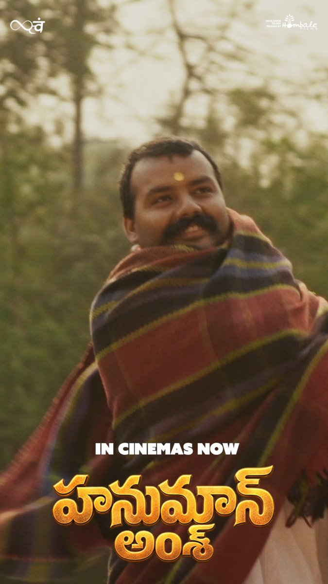 A man with a tilak on his forehead smiles warmly while wrapped in a striped shawl against a backdrop of trees, promoting the Telugu release of the film with text reading "IN CINEMAS NOW" and "హనుమాన్ అంశ" (Hanuman Ansh), aligning with the post celebrating the film's theatrical release across the Telugu states.