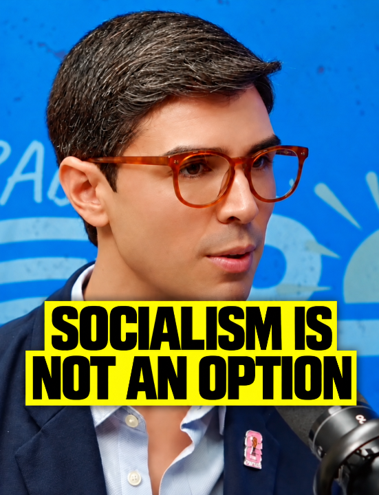 A man with dark hair and a blue blazer is shown in front of a blue background with yellow text overlay reading "SOCIALISM IS NOT AN OPTION".