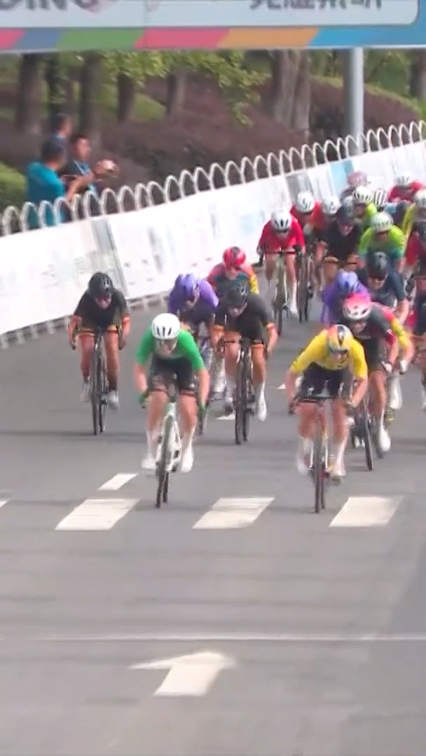 A peloton of cyclists racing toward the finish line on a city street, with two riders in green and yellow jerseys leading the sprint.