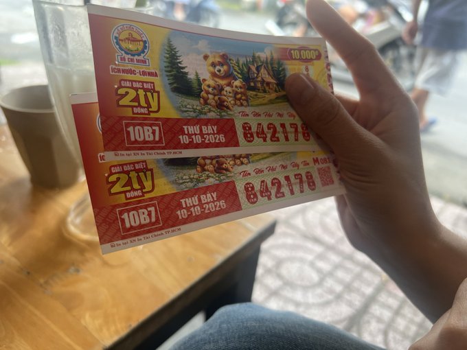A person holds two Vietnamese lottery tickets showing 'GIẢI ĐẶC BIỆT 2 TỶ ĐỒNG', ticket number 10B7, dated 10-10-2026, with series number 842178.