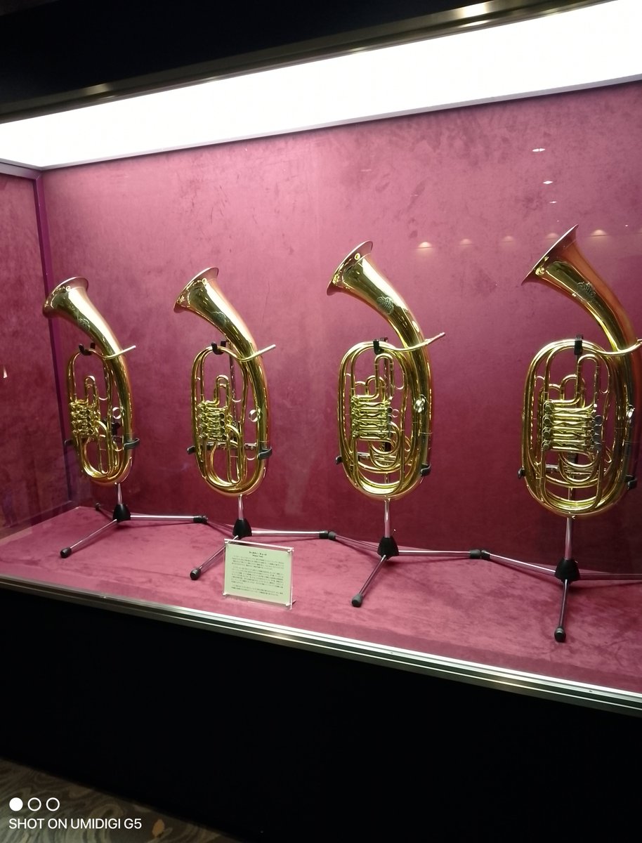 JT75204697's tweet photo. 四コマ『ワグナーチューバのお留守番』

ススム「トリフォニーホールに展示されているワグナーチューバです。本拠地の新日本フィルハーモニー管弦楽団の演目中にワグナーチューバを使う作品がある日はこの展示品が使われる事があります。本日はなかなかレア作品のブルックナー交響曲 第６番です。」
とも子「ブルックナーの交響曲第6番の演奏、とても楽しみですね！
実は、ブルックナーの交響曲でワーグナーチューバが使用されるのは第7番、第8番、第9番の3曲（および『テ・デウム』等）で、第6番の編成にはワーグナーチューバは含まれていません（通常のホルン4本とテューバ1本という編成です）。
そのため、本日の展示ケースのワーグナーチューバたちは、今日はお留守番でじっくり鑑賞できる貴重な機会かもしれません。第6番ならではの明快で独特な��ズムと深みのある響きを、ぜひ存分にお楽しみください！」