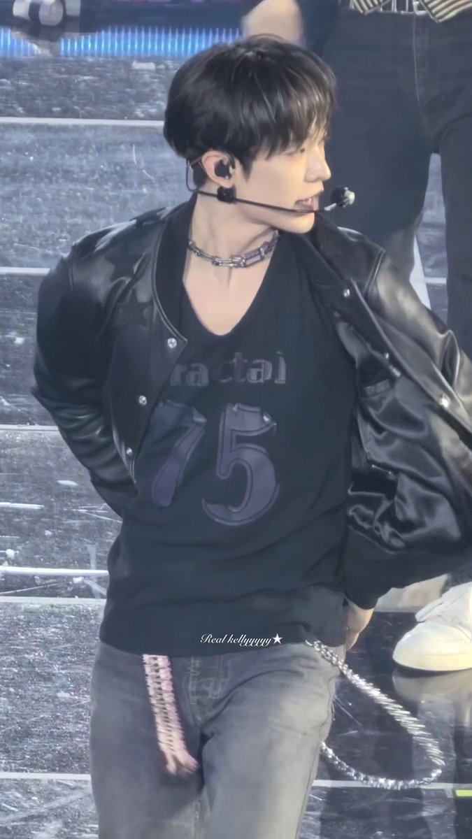 A performer on stage wearing a black leather jacket and a black shirt with "racted" and "75" printed on it, along with a chain necklace and headset microphone. The hashtags indicate this is Yushi from NCT WISH performing "ISPY" at a concert on October 10, 2026.