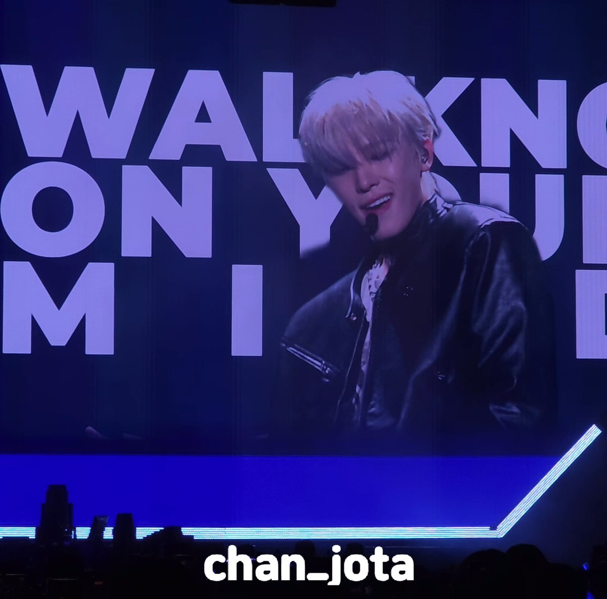 A performer with light-colored hair performs on stage under purple lighting with 'WALKING ON Y' visible on the large screen behind, credited to 'chan_iota'.