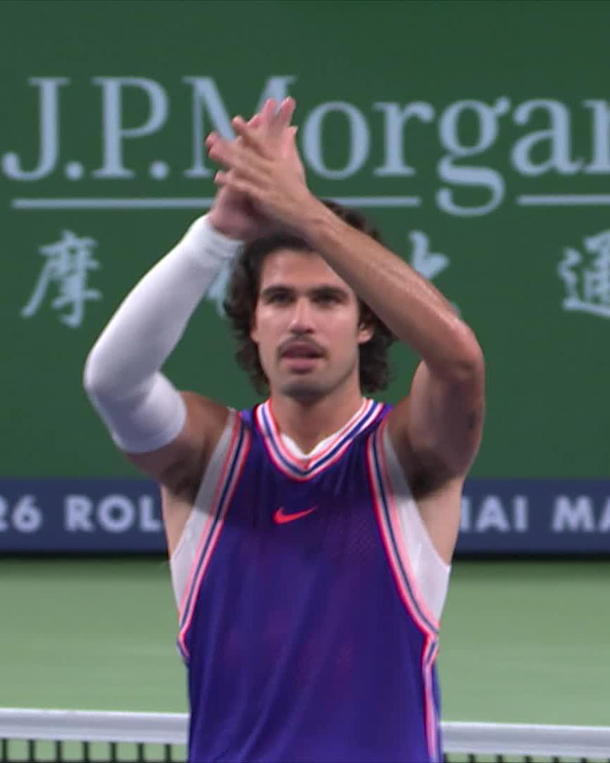 A male tennis player with curly dark hair clapping his hands above his head, wearing a purple Nike jersey, with JPMorgan and Shanghai Masters signage visible in the background.