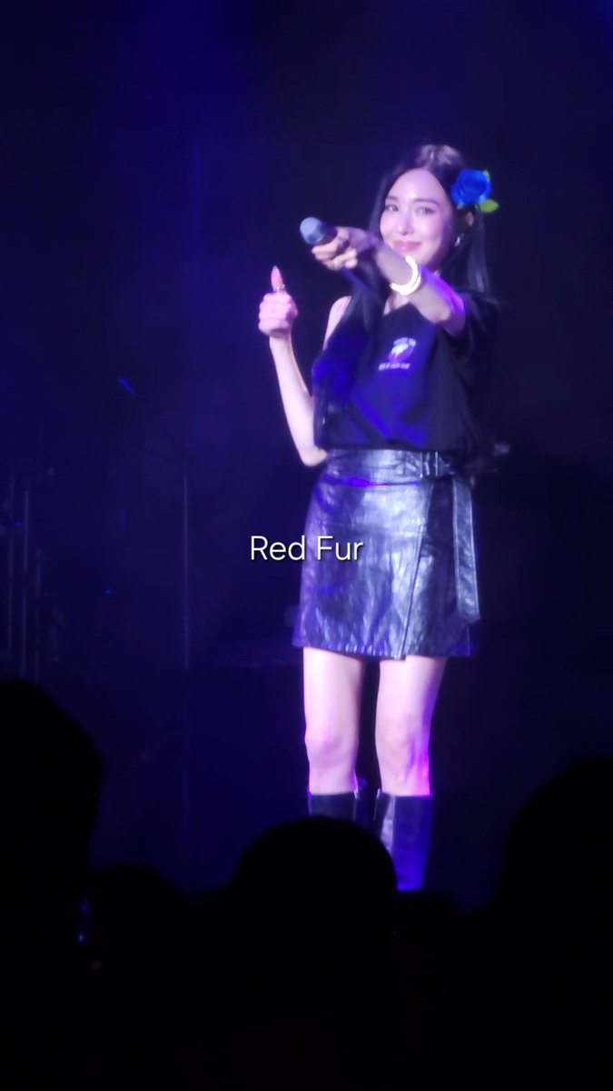 A female performer on stage, wearing a black top and metallic blue skirt, holds a microphone and gives a thumbs-up under purple lighting, with the text 'Red Fur' overlaid.