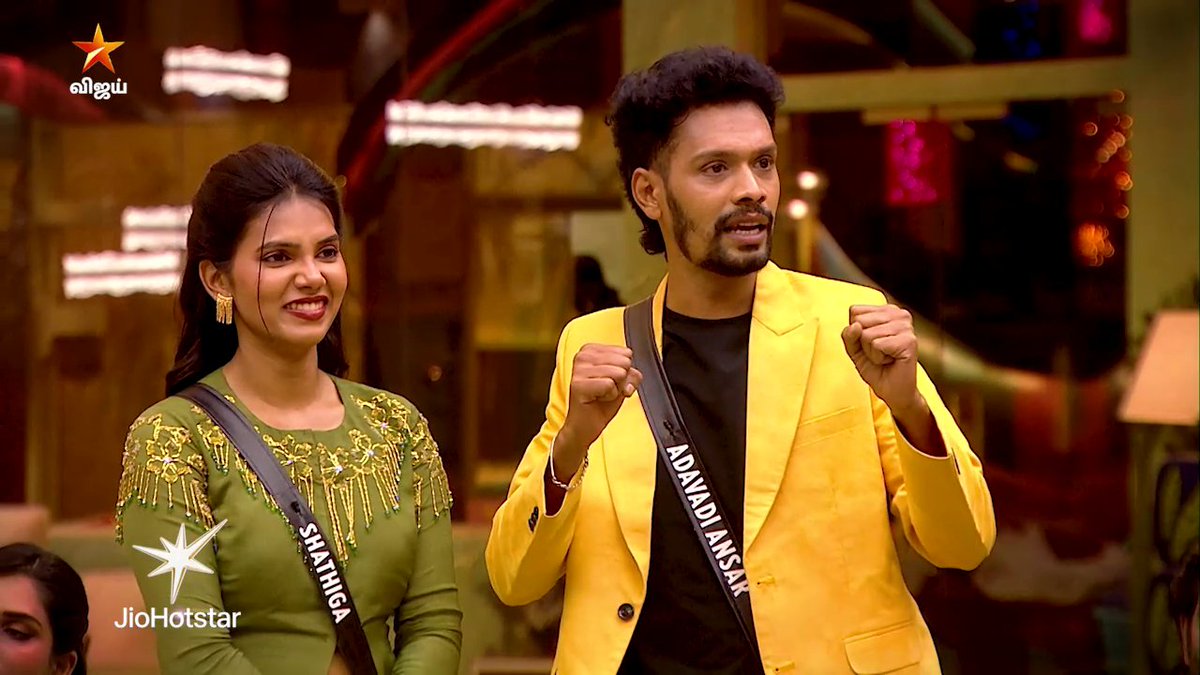 A promotional image for Bigg Boss Tamil Season 10 featuring contestants Shanica (in a green embroidered dress) and AdaiyAnsaR (in a bright yellow blazer), shown celebrating enthusiastically with raised fists. The Vijay TV logo and JioHotstar branding appear in the corners, promoting the show's 9:30 PM airing.