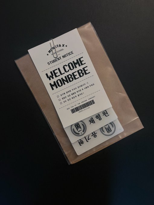 A 'Welcome Monbebe' student notice from Monsta X High School clipped to a brown paper envelope, with Korean text and concert ticket details.