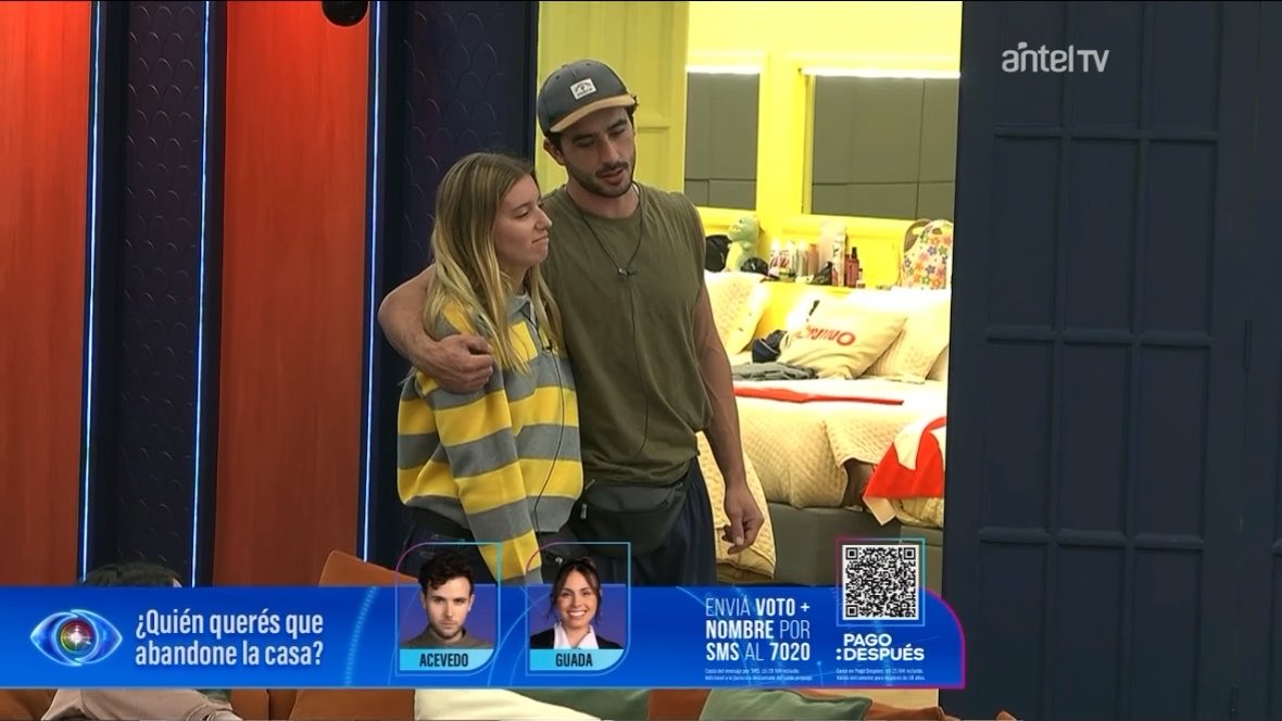 A scene from a reality TV show on 'antel tv' showing a couple standing together, with a voting banner asking '¿Quién querés que abandone la casa?' between contestants Acevedo and Guada.
