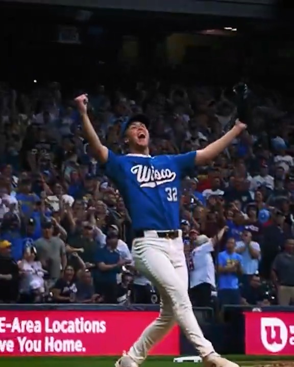 A Milwaukee Brewers player wearing jersey number 32 celebrates triumphantly with both arms raised in front of a packed stadium crowd. The image captures the team's postseason success, complementing the caption's announcement of their best record in baseball and second consecutive NLCS appearance.
