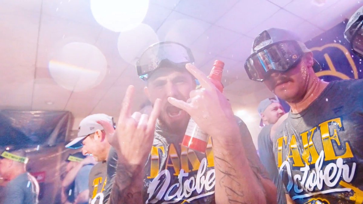 Two celebrating athletes wearing "LAKE OCTOBER" jerseys and ski goggles throw up rock-on hand signs and hold a pink bottle in a champagne-soaked locker room, capturing the exuberant post-championship celebration that inspired the "never rains in Southern California" #WinOurWay caption.