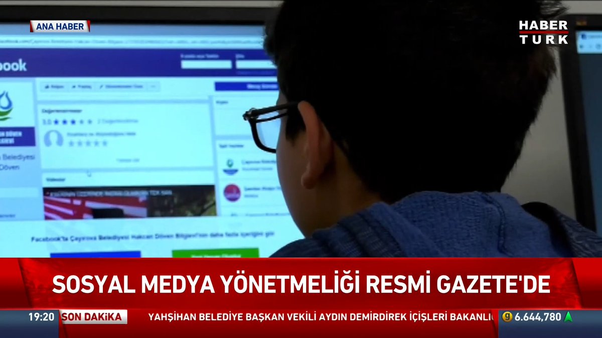 A young man wearing glasses views a social media platform on a computer screen, shown from behind. The Habertürk news broadcast displays the headline "SOSYAL MEDYA YÖNETMELİĞİ RESMİ GAZETE'DE" (Social Media Regulation in the Official Gazette), with breaking news text mentioning a ban on social media for those under 15 effective November 1.