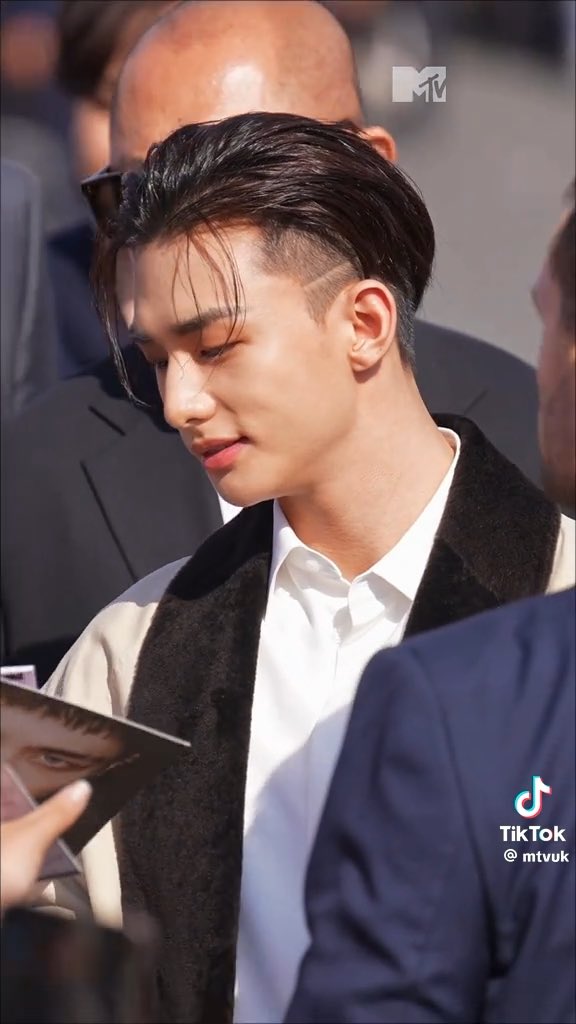 A young man with dark hair wearing a white shirt and black vest looks downward at a photo being handed to him, with an MTV logo visible.