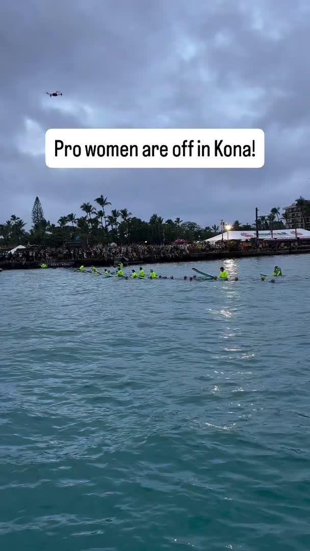 A water-based sporting event captioned 'Pro women are off in Kona!' showing athletes in the water with spectators lined along the shore and a helicopter overhead.