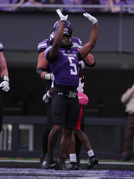Football players in purple Northwestern University jerseys (Big Ten) celebrate on the field, with one player wearing number 5 raising his arms.