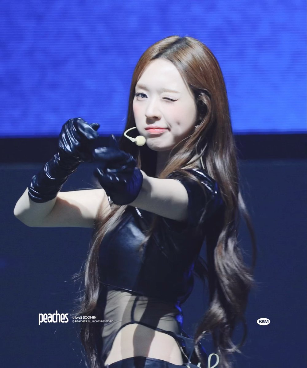 A performer winks at the camera on stage, wearing a black outfit with long black gloves and a headset microphone; the watermark reads 'peaches tripleS SOOMIN © PEACHES ALL RIGHTS RESERVED' alongside a 'KSM' logo.