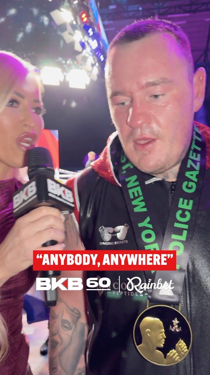 A man being interviewed at BKB 69 with the quote "ANYBODY, ANYWHERE" displayed; he wears a jacket with a police gazette strap and a championship belt buckle.