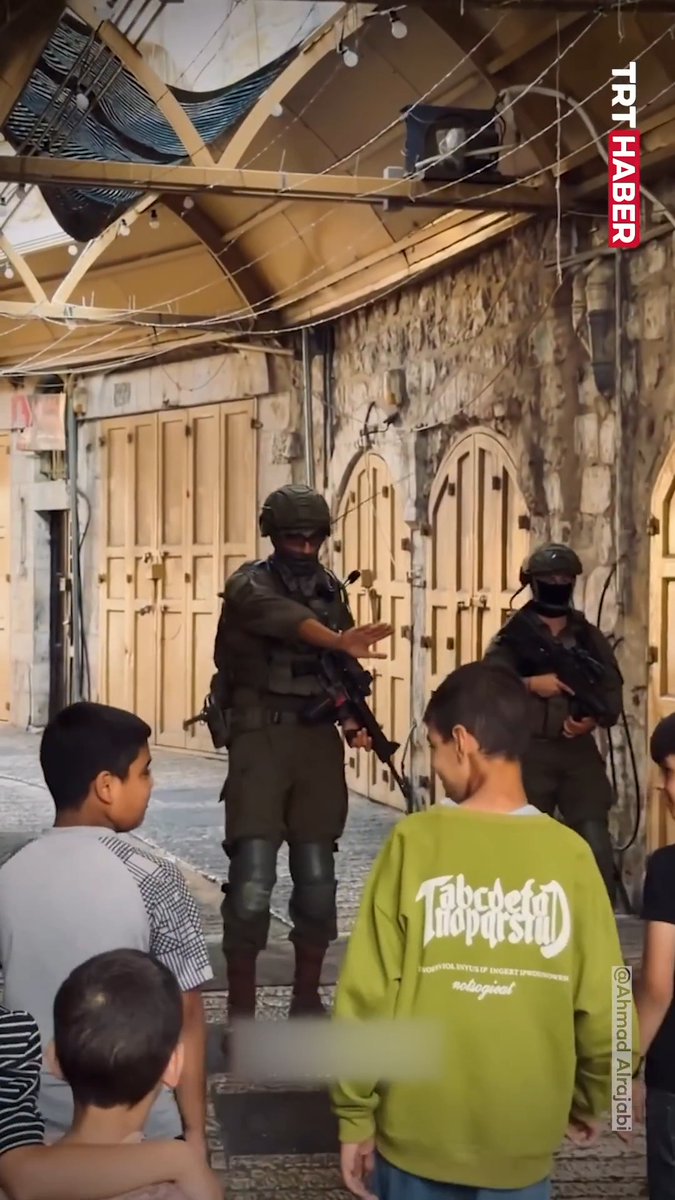 Photograph showing armed soldiers in tactical gear standing in a street with children nearby, watermarked 'TRT HABER' with credit '@Ahmad Alrobi'.