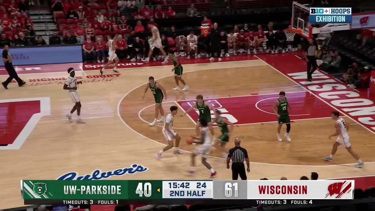 A Wisconsin basketball player in white drives toward the hoop against UW-Parkside defenders in green during an exhibition game, with Wisconsin leading 61-40 at 15:42 in the second half. The image illustrates "Big Vic's" dominant performance referenced in the caption, showing him in active play.