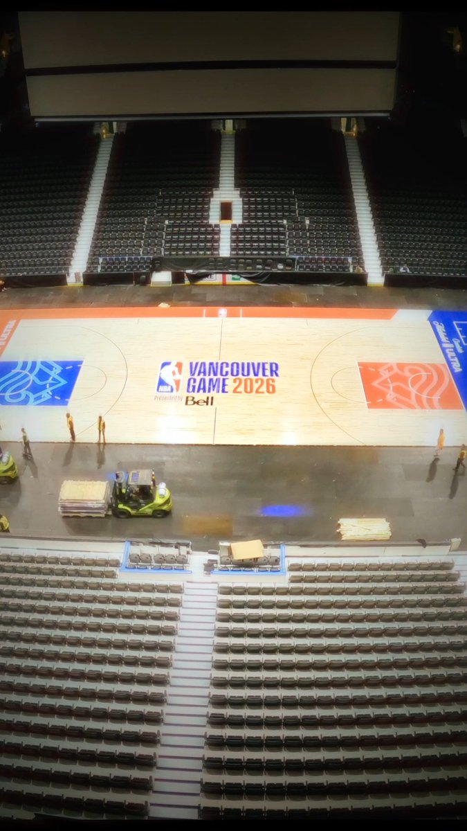 A view from the upper seats of an arena showing the basketball court below with "Vancouver Game 2026" presented by Bell branding at center court, while workers and a forklift prepare the floor.