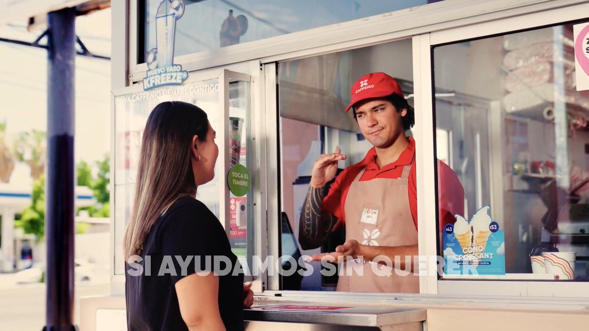 An advertisement showing a customer at a Caffenio kiosk interacting with an employee in a red uniform and cap. Text reads 'SI AYUDAMOS SIN QUERER', 'NUEVO VASO KFREEZE', and 'UMI CONO CROSSANT'.
