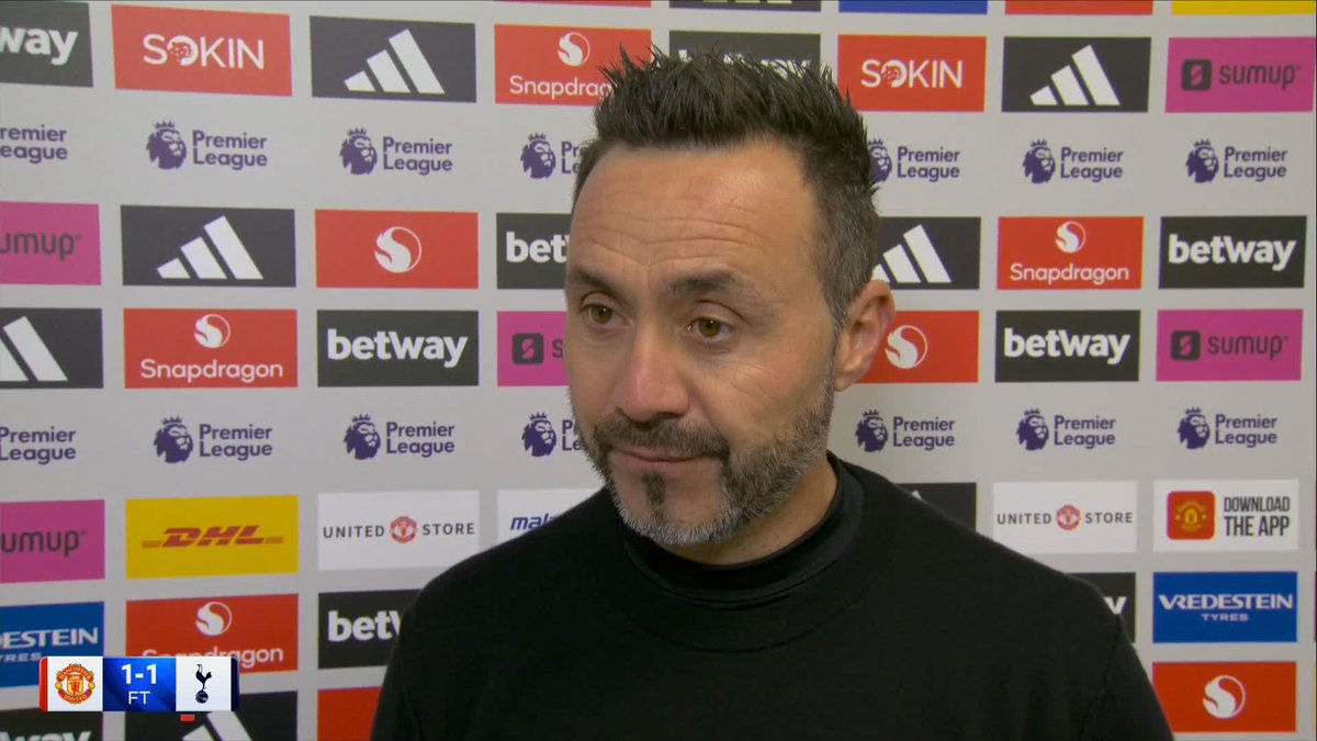 A man with short dark hair and a trimmed beard, appearing to be Roberto De Zerbi, is being interviewed against a backdrop featuring Premier League and sponsor logos including Snapdragon, Adidas, betway, DHL, and SumUp. The scoreboard in the corner shows a 1-1 FT result between Manchester United and Tottenham, with Spurs' crest displayed.