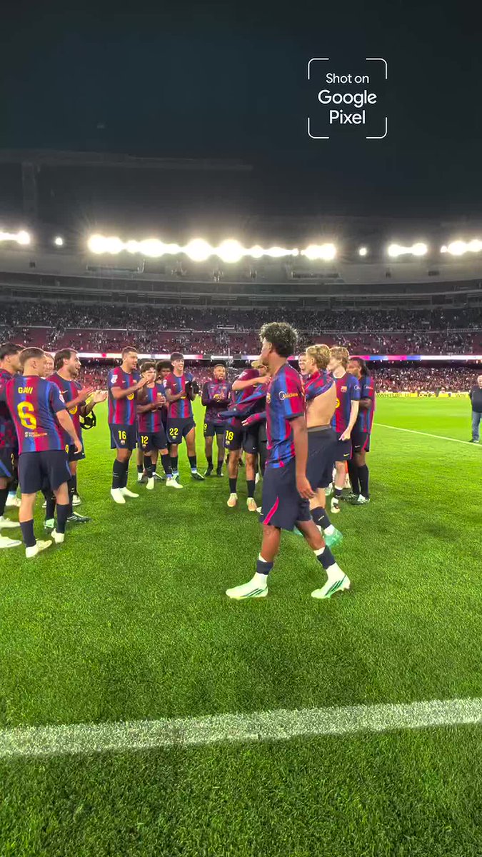 FC Barcelona players in their blue and red striped jerseys gather on a green pitch inside a large stadium at night, celebrating with one player holding a jersey, with a 'Shot on Google Pixel' watermark visible.