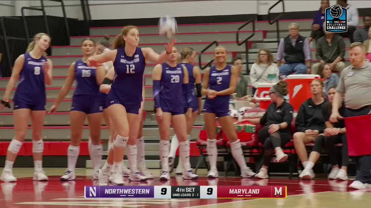 A Northwestern volleyball player (jersey #12) prepares to serve during the 4th set of a match against Maryland, with Northwestern trailing 9-9 and UMd leading 2-1.