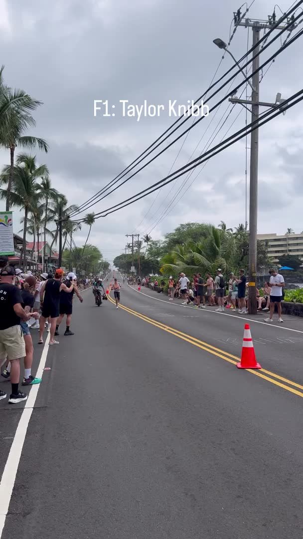 A runner competes in a race on a palm-lined tropical road, with text overlay reading 'F1: Taylor Knibb' and spectators watching from the sidelines behind an orange traffic cone.