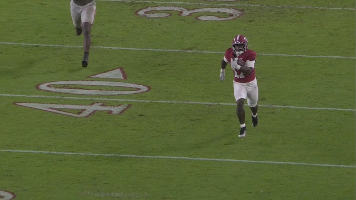 A football player in an Alabama crimson and white uniform sprints down the field with the ball tucked securely in his arm, with the "40" yard line marker visible on the green turf. The image captures the Crimson Tide scoring play referenced in the caption about Alabama getting on the board.