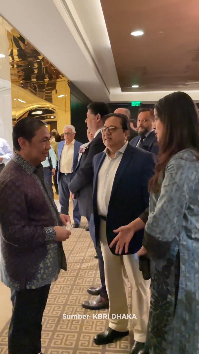 A group of people, including a man in a blue blazer and white pants, standing and conversing in a hallway, with text 'Sumber: KBRI DHAKA' at the bottom.