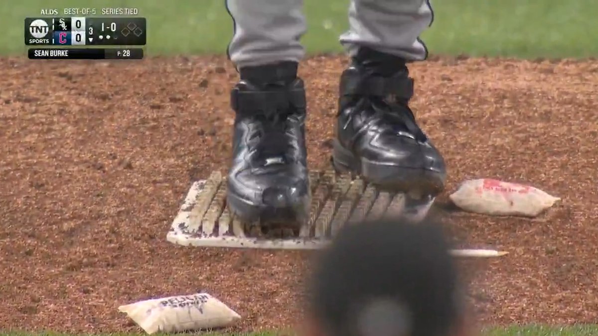 A close-up shot from an ALDS Best-of-5 broadcast shows a player wearing black Nike Air Force 1 cleats on the pitcher's mound, with the on-screen graphic indicating Sean Burke has thrown 28 pitches in a scoreless tie game between the Chicago White Sox and Cleveland Guardians. Rosin bags lie scattered on the dirt around the metal pitching rubber beneath his feet.