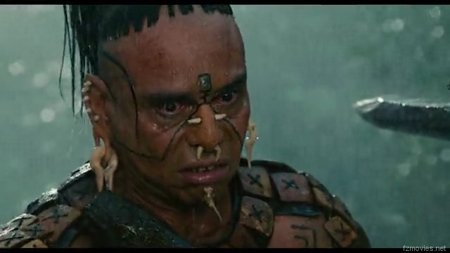 Close-up shot of a warrior character with facial scars, a top-knot hairstyle, and bone piercings, with a blade visible near his face, sourced from fzmovies.net.