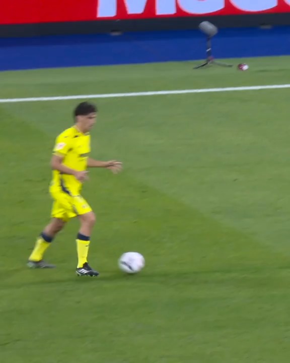 A Real Madrid player in a yellow away kit prepares to strike the ball during a La Liga match against Villarreal, with a microphone visible in the background suggesting broadcast coverage of the highlights. The image aligns with the caption referencing Courtois (Real Madrid's goalkeeper) and the Real Madrid vs. Villarreal La Liga encounter.