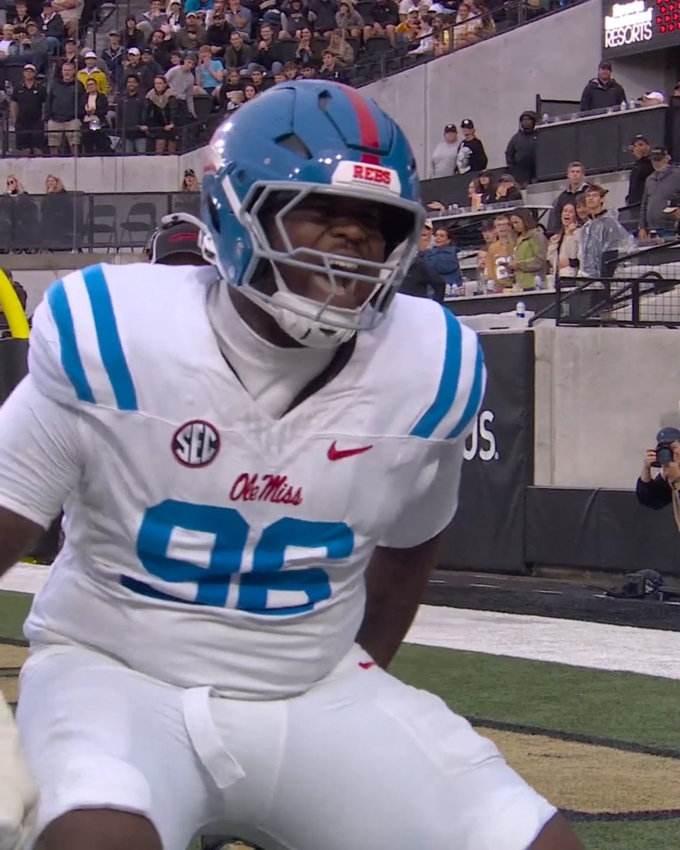 An Ole Miss football player wearing a white jersey with the number 22 and a blue helmet featuring the SEC logo is shown on the field with spectators visible in the background.