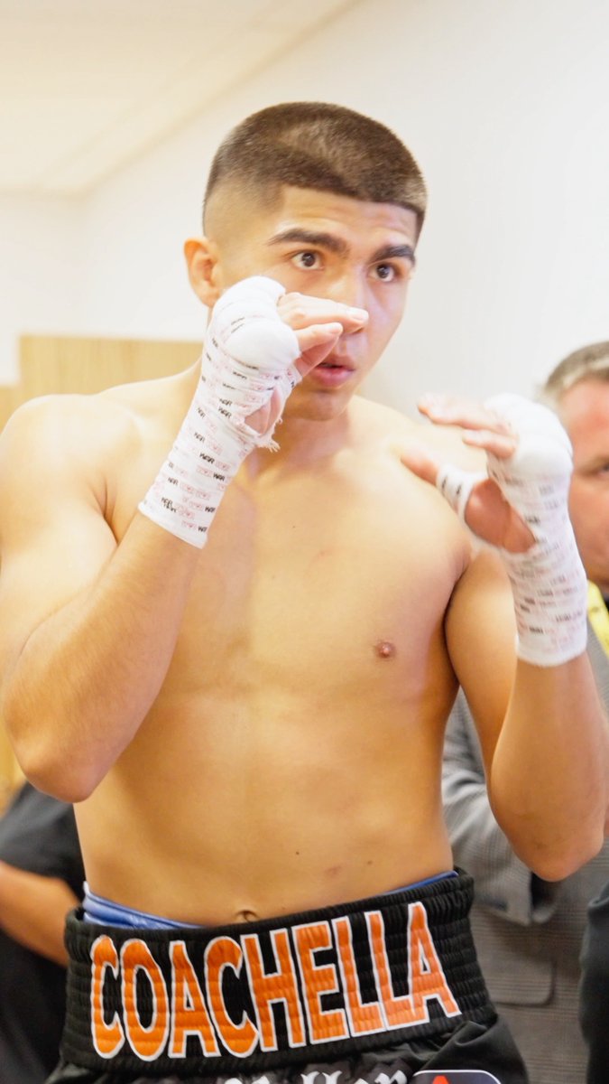 A young boxer with hand wraps stands in fighting stance, wearing black trunks emblazoned with "COACHELLA" in bold orange lettering, ready to compete. The post identifies him as Grant Flores preparing for fight night in Chicago, with the bout aired on DAZN.