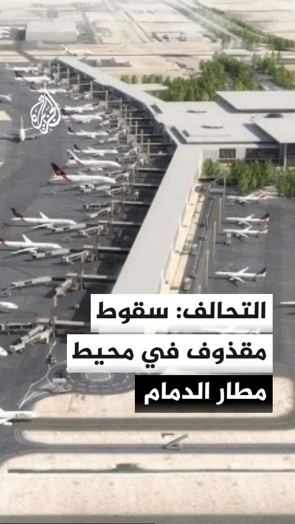 An aerial view of King Fahd International Airport in Dammam, Saudi Arabia, showing multiple commercial aircraft parked at the terminals and taxiways, with Arabic text overlay reading "التحالف: سقوط مقذوف في محيط مطار الدمام" (The Coalition: A projectile fell in the vicinity of Dammam Airport), relating to the news of a projectile reportedly landing near the airport with no reported casualties or damage.