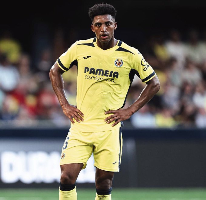 Alex Freeman stands in Villarreal's yellow away kit featuring the "PAMESA cerámica" sponsor and the number 6 on his shorts, appearing composed with hands on hips during a match against Real Madrid. The image visually complements the caption highlighting his standout defensive performance with an 8.4 rating, despite the team's loss.