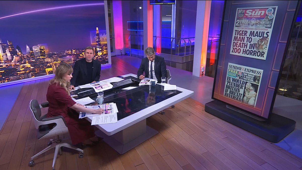 Three news anchors sit at a desk in a studio with a London skyline backdrop, reviewing Sunday newspapers including The Sun ('TIGER MAULS MAN TO DEATH IN ZOO HORROR') and Sunday Express ('EU WOULD PUNDER BRITAIN IF BREXIT REVERSED').