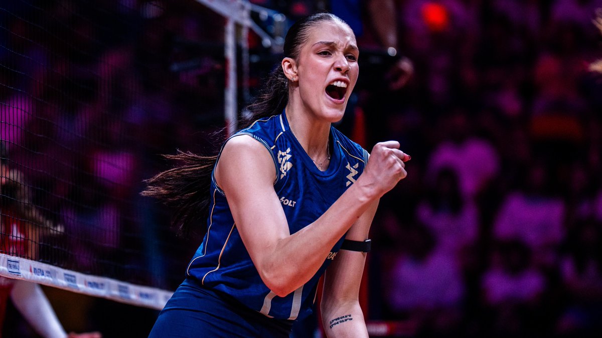 A female volleyball player in a blue jersey with a Mizuno logo celebrates passionately near the net, her fist raised and mouth open in a triumphant shout, with "BOLT" visible on her uniform. The image captures the intensity and emotion of a competitive match, fitting the accompanying post about Brazil's Luzia joining Minas Tênis Clube for her first season at "Rua da Bahia."